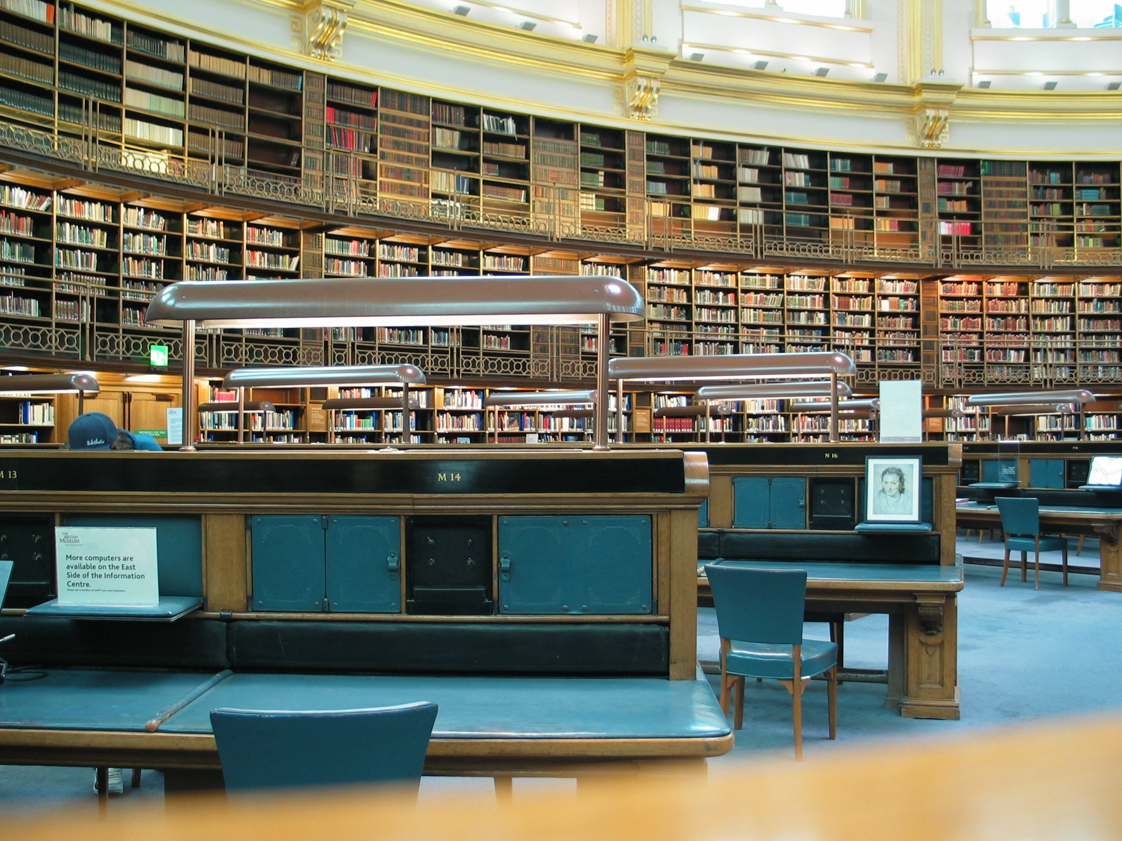 Reading desks and lamps inside the British Museum Reading Room, with desk M14 closest to the viewer.